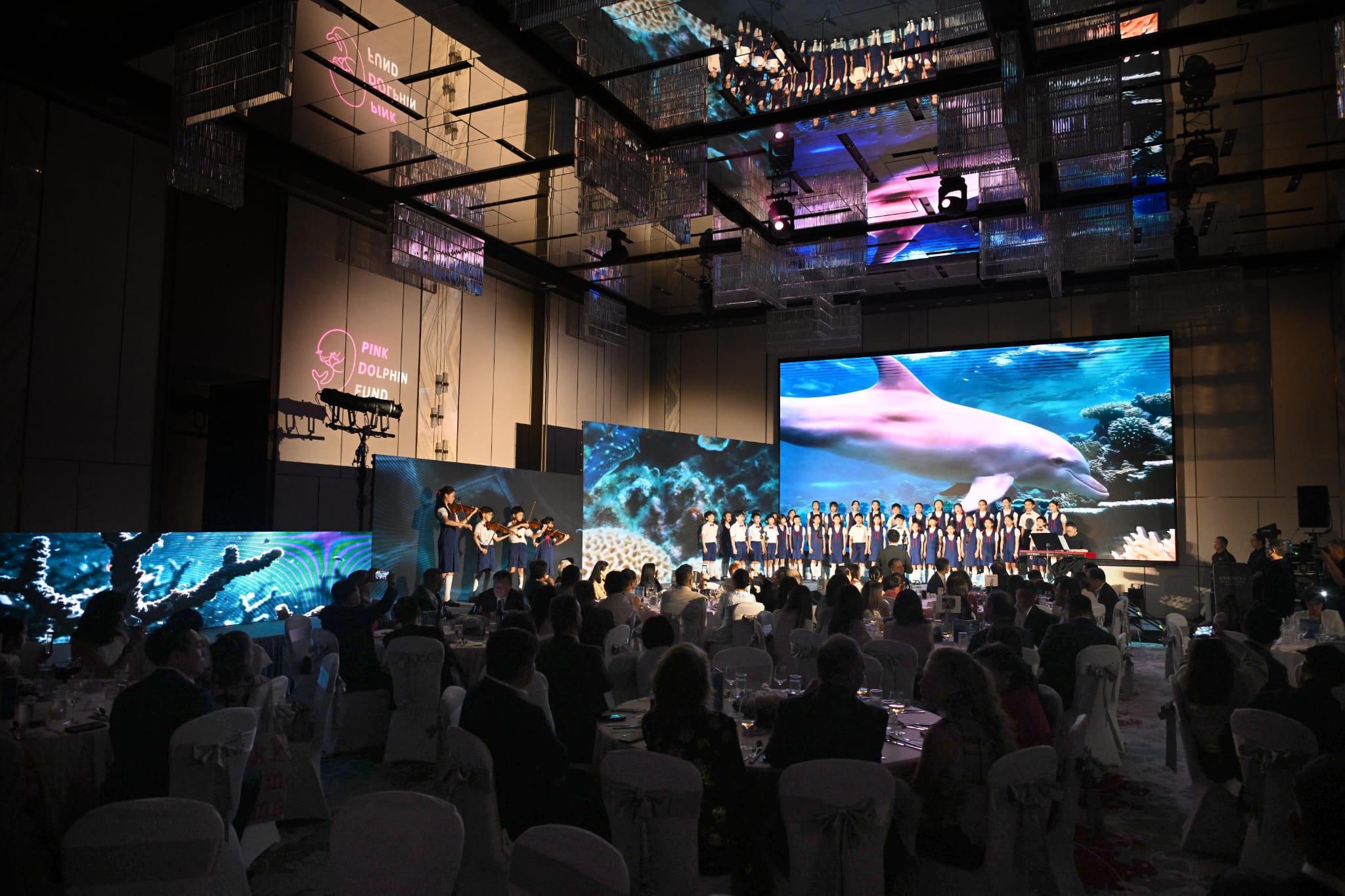 Student choir performance at Pink Dolphin Award ceremony with ocean-themed LED displays